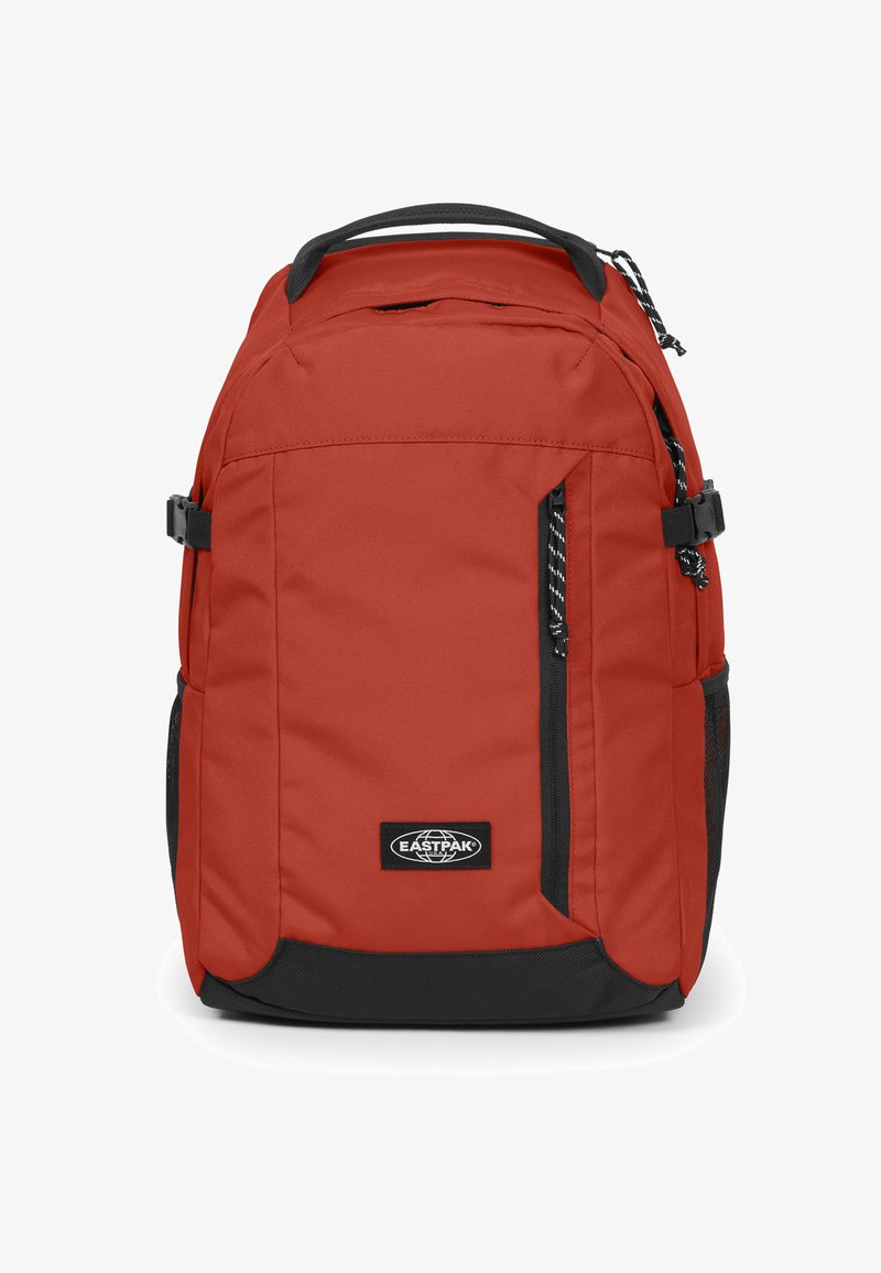 Zaino di tessuto rosso con base nera, dotato di tasche laterali, una parte anteriore con zip e una toppa con logo. Include spallacci regolabili e maniglia superiore.