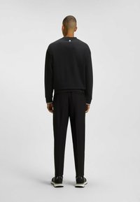 Sudadera negra con un acabado texturizado, que presenta un pequeño logo en el cuello. Combinada con pantalones negros ajustados y zapatillas negras.