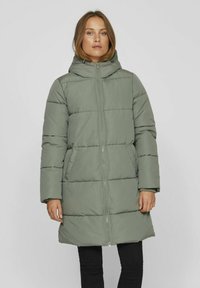 Manteau rembourré vert avec une fermeture éclair intégrale, une capuche et des poches latérales. Il présente une silhouette ample et un design matelassé.