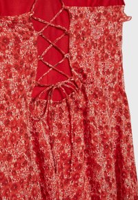 Robe rouge à fleurs avec détail de dos lacé croisé et fines bretelles.