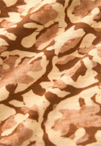 Primo piano di un morbido tessuto con un motivo astratto a stampa animale nei toni del marrone e del beige, che mostra la texture e lievi pieghe.