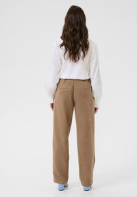 Pantalon en velours côtelé marron avec une taille haute et des jambes larges, associé à une chemise blanche ornée de broderies florales bleu clair sur les manches.