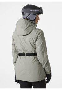 Hellgraue, isolierte Skijacke mit Kapuze, tailliertem Schnitt und schwarzem Gürtel. Schwarze Handschuhe und Helm sind sichtbar, glatte Textur, praktisches Design.