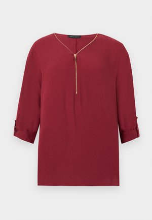 Bluză burgund cu mâneci lungi, fermoar auriu pe jumătate și manșete întoarse, având decolteu în V și croială lejeră.