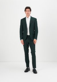 Dark green suit made of smooth fabric, featuring a single-breasted jacket with notch lapels, matching pants, and a white dress shirt underneath.