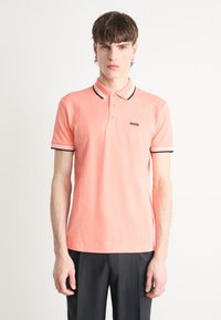 Polohemd in Koralle mit einer Knopfleiste mit zwei Knöpfen, kurzen Ärmeln und kontrastierendem Kragen. Verfügt über ein schwarzes Logo auf der Brust. Aus Baumwollmaterial.