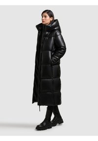Cappotto imbottito nero con una silhouette lunga e oversize, caratterizzato da un colletto alto, un design trapuntato, chiusura con zip e tasche laterali.