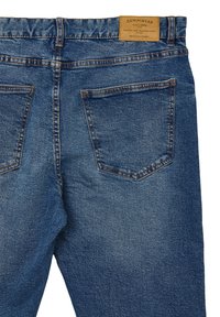 Jeans in denim con un lavaggio blu medio, dotati di due tasche posteriori, cuciture arancioni e una etichetta in pelle marchiata in vita.