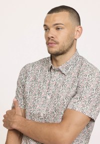 Chemise à manches courtes avec boutons en tissu léger, arborant un motif abstrait multicolore rouge, vert et noir sur un fond clair.