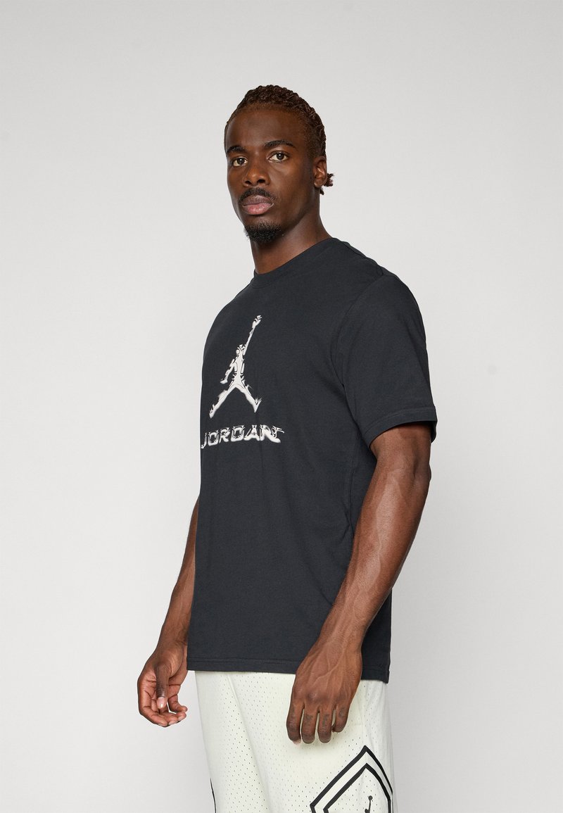 Sort bomulds t-shirt med et stort hvidt Jordan-logo på forsiden, med rund hals og korte ærmer, vist med lyse shorts.