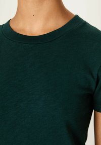 Temno zelena kratka majica s kratkimi rokavi, izdelana iz mehke bombažne tkanine, z klasičnim okroglim izrezom in gladko teksturo.