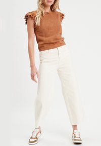 Haut court marron texturé avec accents de manches en dentelle, jean crème à jambes larges, et baskets marron et blanches. Tenue décontractée avec des détails distincts.