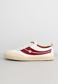 Baskets basses blanches avec semelle et embout beige, avec deux bandes de cuir rouges et un logo "B" doré sur le côté.