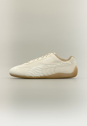 Кремав маратонка на Puma с бежова подметка, странична декорация с вълнообразен мотив и дизайн с връзки, показан в страничен профил на неутрален фон.