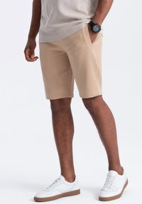Pantaloni corti in misto cotone beige con tasche laterali, una vestibilità comoda e orlo a coste. Abbinate a sneakers bianche con suola in gomma.
