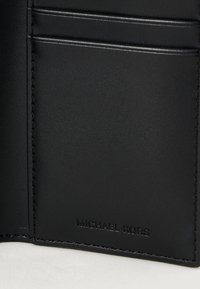 Angolo di un portafoglio in pelle nera con slot per carte visibili, caratterizzato dal logo Michael Kors in rilievo vicino al bordo inferiore.