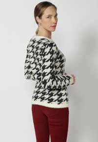 Pulover tricotat cu model houndstooth în negru și ivoriu, cu guler rotund și mâneci lungi. Material moale, texturat.
