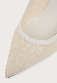 Gros plan d'une chaussure en dentelle crème à bout pointu avec une bordure blanche le long de l'ouverture.