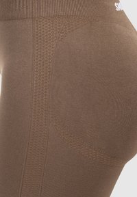 Nahaufnahme von braunen Leggings mit strukturierten Mustern und einem nahtlosen Bund, die die Dehnbarkeit des Stoffes und die Designdetails hervorhebt.