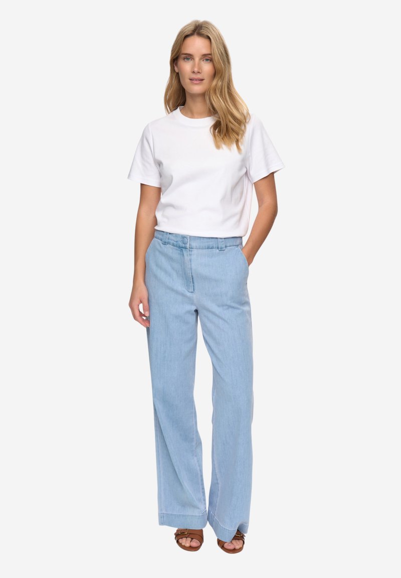 Pantalon large bleu clair à taille haute, associé à un t-shirt blanc ajusté à col rond. Design simple, tissu décontracté et lignes épurées.