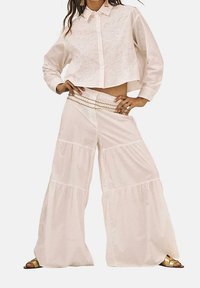 Camisa blanca recortada con bordado, combinada con pantalones de pierna ancha en capas de tela ligera. Incluye un detalle decorativo en la cintura.