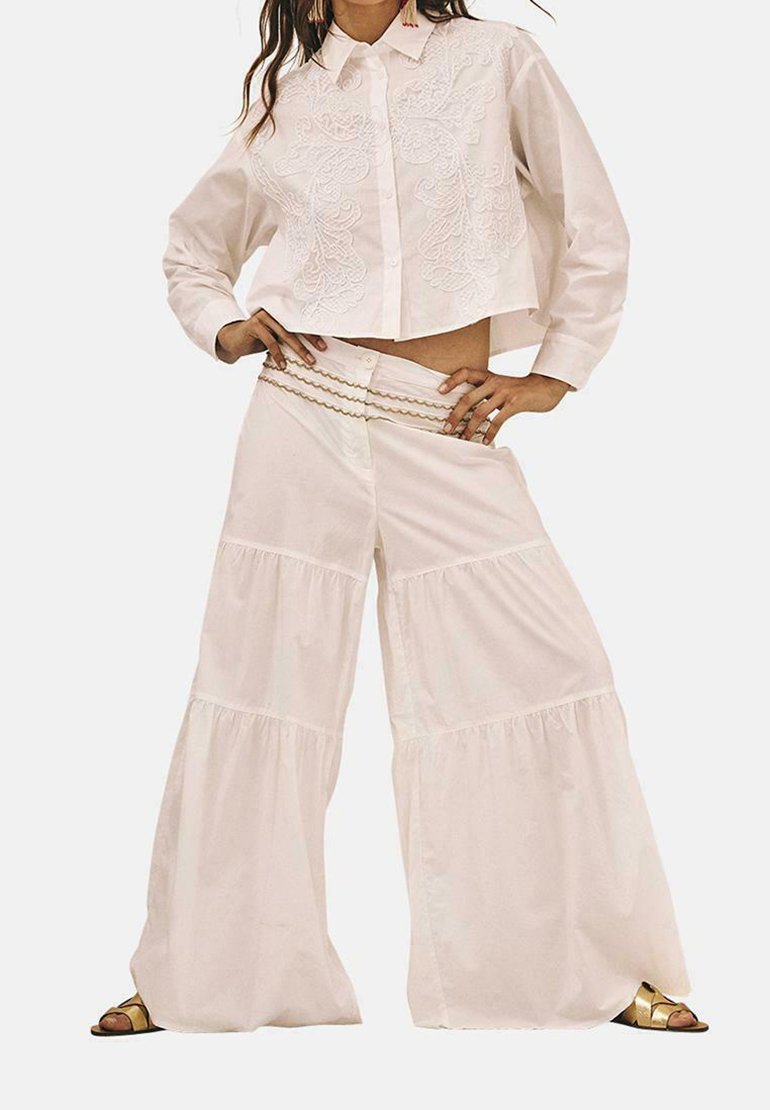 Camisa blanca recortada con bordado, combinada con pantalones de pierna ancha en capas de tela ligera. Incluye un detalle decorativo en la cintura.