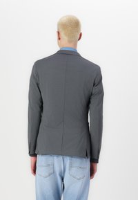 Grijze blazer met een getailleerde pasvorm, enkele split en notch-kragen, gemaakt van glad materiaal. Draag met een lichtblauw overhemd en gecombineerd met denim.