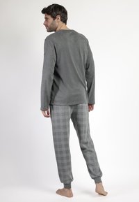 Top gris de manga larga con tejido texturizado, combinado con pantalones de cuadros grises. Los pantalones tienen puños elásticos y un ajuste relajado.