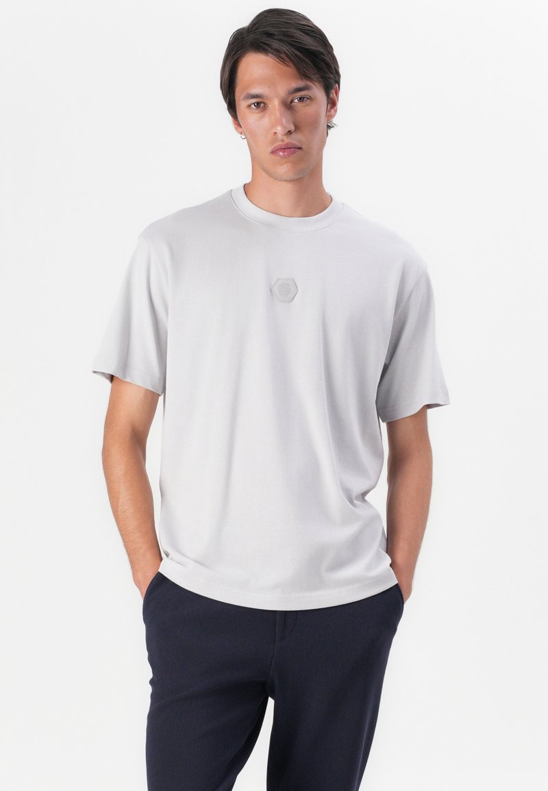 T-shirt grigio chiaro a maniche corte realizzato in tessuto morbido, con un discreto logo esagonale sul petto e un design classico a girocollo.