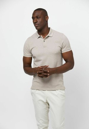 Polo de manga corta color beige con cuello de solapas, con una tapeta de botones; combinado con pantalones de color claro; textura suave.