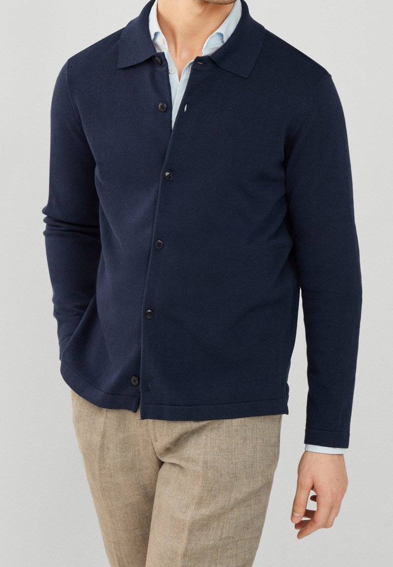 Cardigan blu navy realizzato in tessuto morbido, con collo a punta, chiusura a bottoni frontale e maniche lunghe. Texturizzato con una finitura liscia.