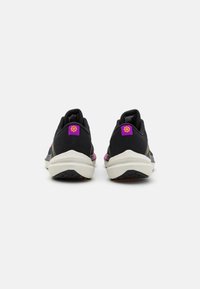 Zapatillas deportivas negras con parte superior texturizada, una media suela blanca y un acento rosa en el talón con un detalle de logo.