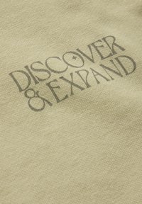 Bomullsduk med en strukturerad yta i ljusgul, med tryckta orden "UPPTÄCK & EXPANDERA" i mörkgrå.