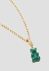 Gul kædedesign med en grøn gummibjørn pendant med en struktureret overflade, prydet med en glitrende diamantslignende ring.