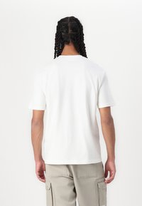 Hvid bomulds t-shirt med løs pasform, korte ærmer og lige kant, båret med lysegrå cargobukser, der viser et enkelt design.