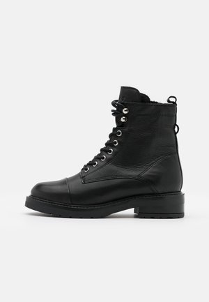 Botte de combat en cuir noir à lacets avec œillets métalliques, bout arrondi, languettes de traction et semelle en caoutchouc épaisse, vue de profil latéral.