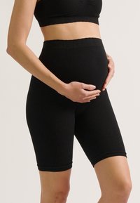 Zwarte zwangerschapsshorts van ribstof, met een elastische tailleband en een knielange snit. Gladde textuur zonder extra patronen.