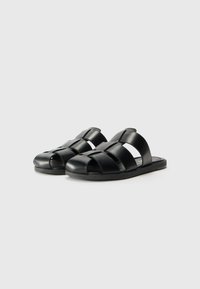 Black leather sandals with open toe design, featuring crisscross straps and a flat sole. Smooth texture with minimalistic accents.