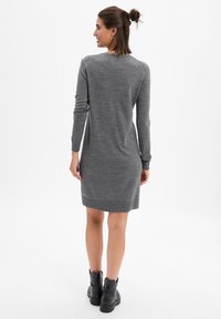 Robe grise à manches longues avec une silhouette ajustée et un ourlet côtelé. Portée avec des bottines noires à la cheville. La texture semble lisse et douce.