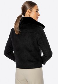 Chaqueta con collar de piel sintética negra con un diseño corto, mangas largas y textura suave. Presenta un acabado liso y líneas limpias.