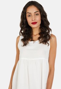Vestido blanco sin mangas hecho de una tela suave, con un corte holgado y detalle fruncido en la cintura. Textura suave y diseño sencillo.