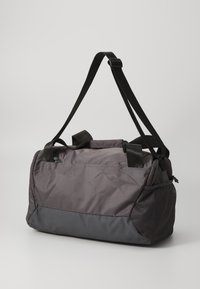 Sac de sport en tissu gris foncé avec une surface texturée, doté de sangles noires, de poignées supérieures et d'une poche en mesh sur un côté.