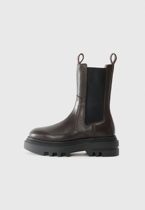 Stivaletto in pelle marrone con pannelli laterali in elastico nero, cuciture a contrasto, linguette e una suola in gomma spessa e texture.