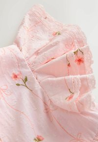 Gaiši rozā auduma kleita ar ziedu izšuvumiem un teksturētām apdrukām. Īpašības ietver viļņainas piedurknes un smalku mežģīņu apdari gar malām.