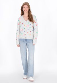 Cárdigan gris con patrones de corazones coloridos, textura suave, cuello en V y botones de madera. Combinado con jeans azul claro y zapatillas blancas.