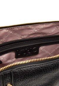 Intérieur d'un sac en cuir noir avec une finition texturée, doté d'une doublure rose à motifs et d'une fermeture éclair dorée. Logo embossé sur une étiquette en cuir.