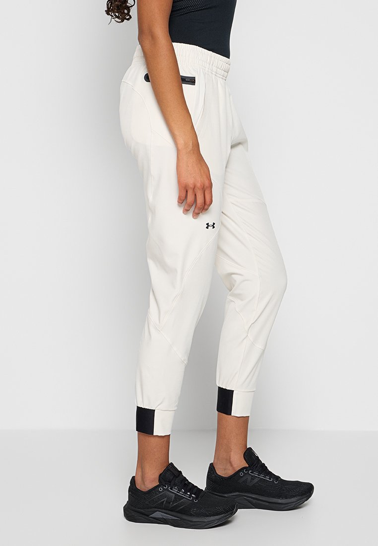 Persona che indossa pantaloni jogger bianchi a tapered con polsini neri e sneakers nere, in piedi contro uno sfondo chiaro e semplice.