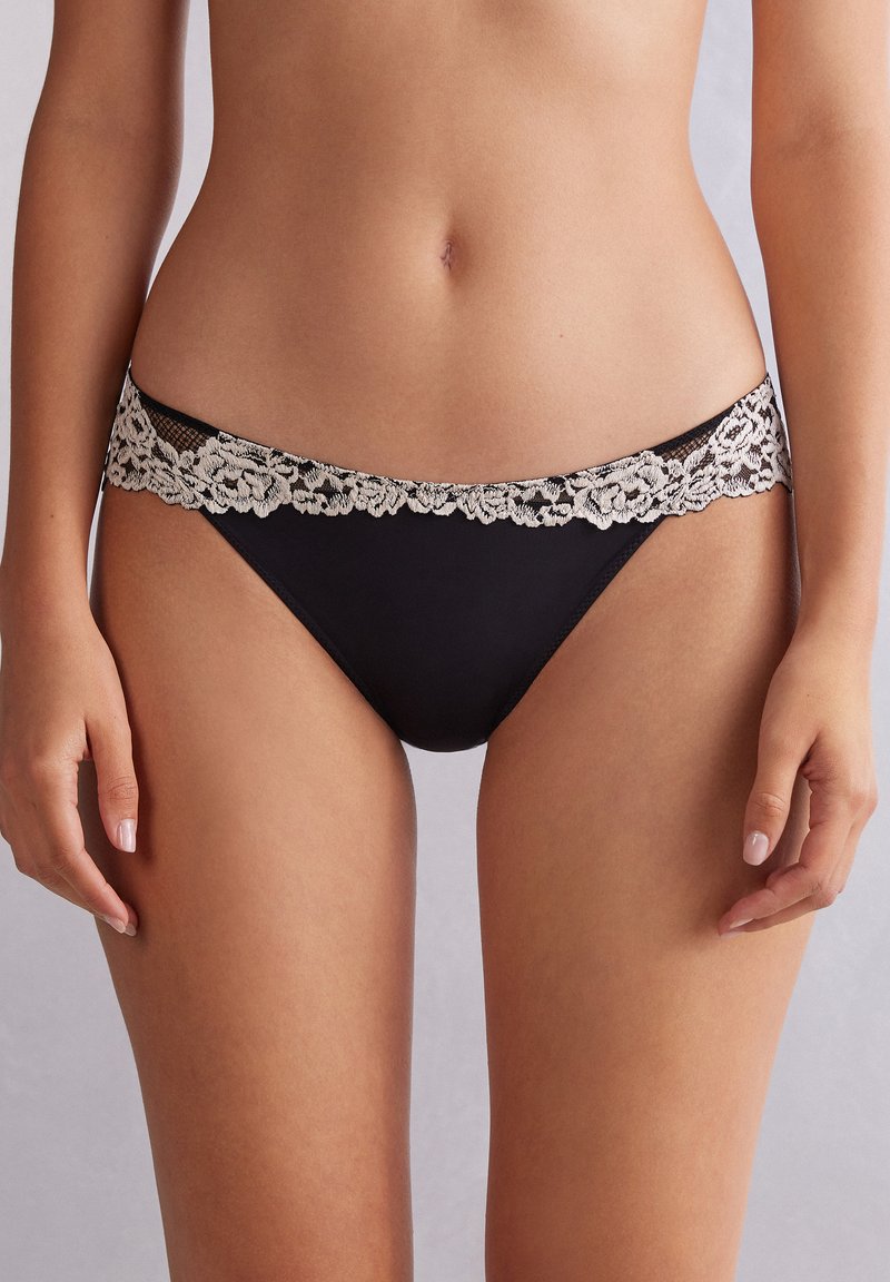 Zwarte bikini slips met een bloemenkant tailleband, voorzien van een gladde textuur en een lage taille. Verstelbare en comfortabele pasvorm.