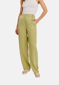 Světlé zelené kalhoty širokého střihu vyrobené z hladké látky, s vysokým pasem a dvěma bočními kapsami, doplněné béžovými teniskami.