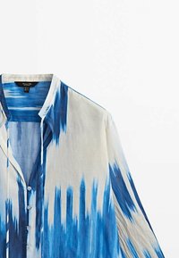 Sininen ja valkoinen liukuvärjätty paita, valmistettu kevyestä kankaasta. Siinä on napitettava rintalista, levitetty kaulus ja pitkät hihat, joissa on hillittyjä kuvioita.